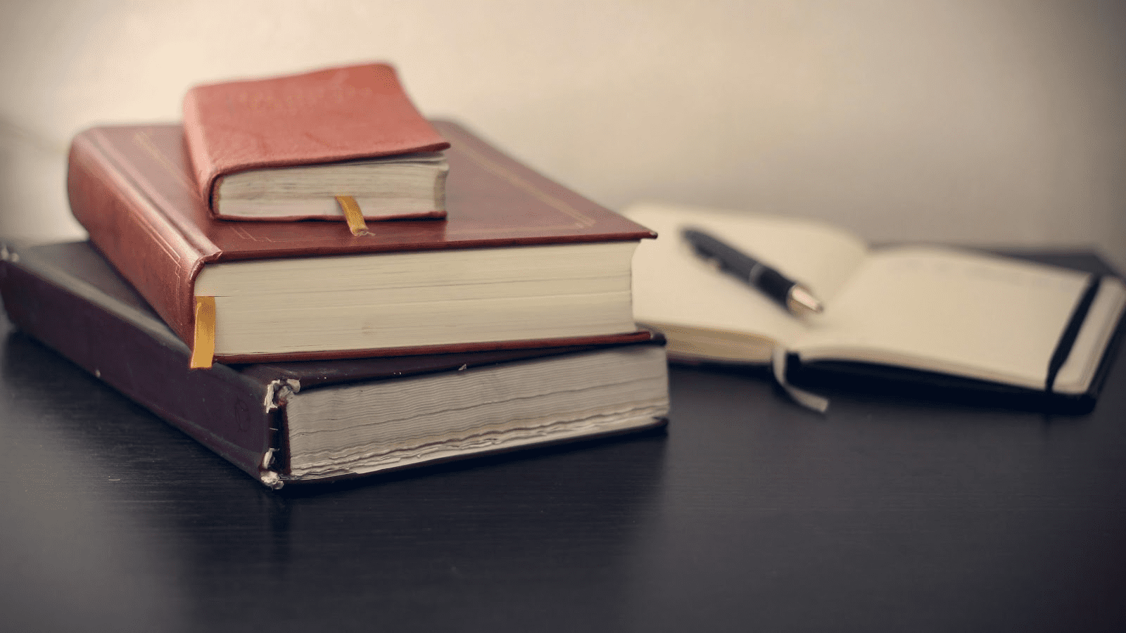 Three books lay beside an opened notebook and pen.